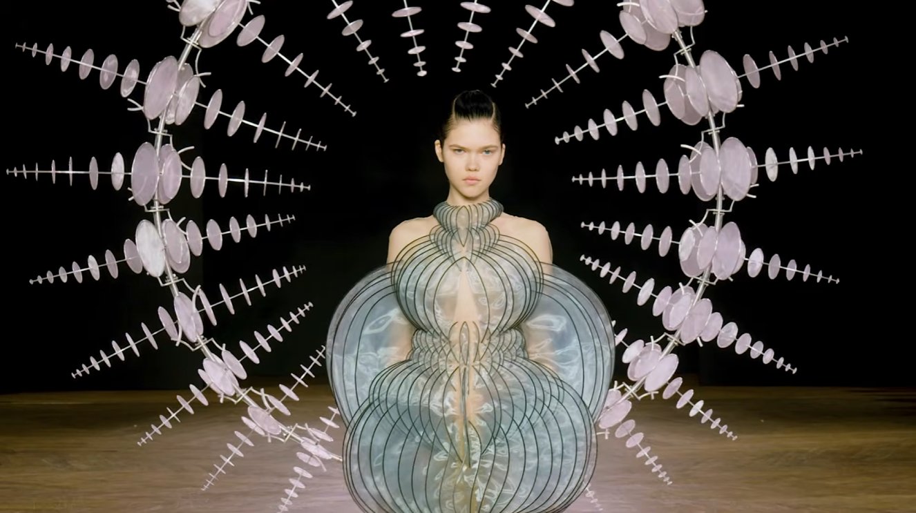 The finale "Infinity" dress now lives in a museum. The V&A in London acquired it, and their own writeup notes it was partly inspired by van Herpen's visits to CERN, the physics research facility where scientists study the fundamental origins of matter, tying literal particle physics into a couture gown.